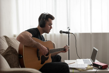 Male songwriter playing guitar on sofa