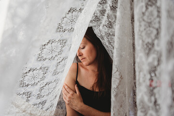 Beautiful woman with long brown hair surrounded by lace curtains.