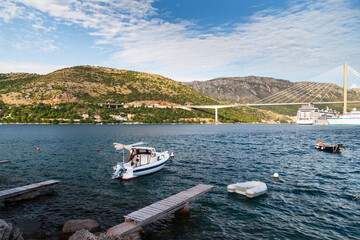 Fototapeta premium Fantastic croatian seascape with narrow wooden bridge and small boat at sunset. Dubrovnik, Croatia. Travel concept.