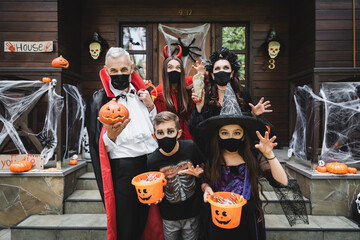 family in creepy costumes and black medical masks near house with halloween decoration