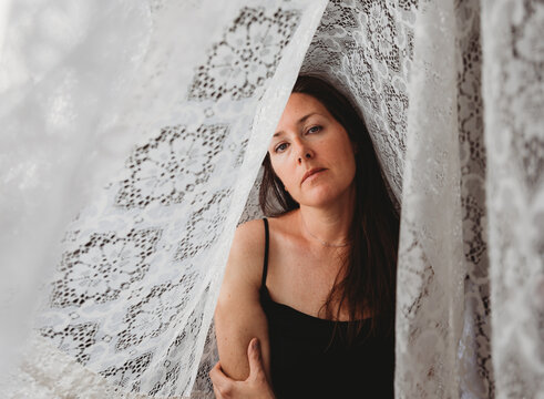 Beautiful woman with long brown hair surrounded by lace curtains.