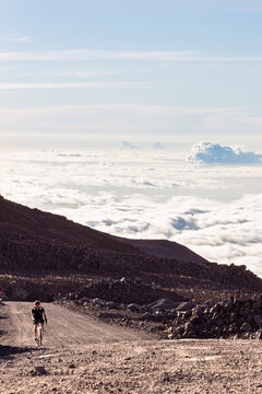 Male cyclist climbs road above cloud up Mauna Kea volcano, Hawaii