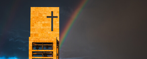 A rainbow above a modern church tower with christian cross, image with copy-space, banner