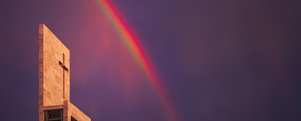 A rainbow above a modern church tower with christian cross, image with copy-space, banner