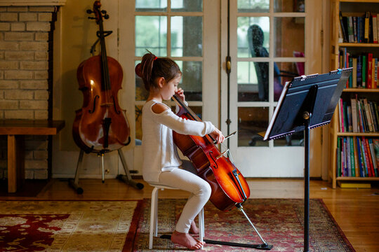 a focused graceful child practices cello in window light at home