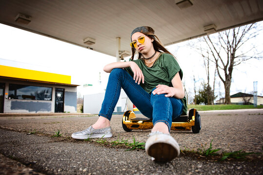 Cool tween girl with blond hair and sunglassess sitting on hoverboard