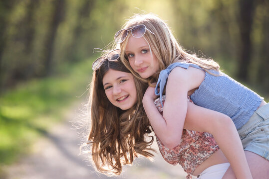 Two happy beautiful young teen girls on sunny treelined country road.