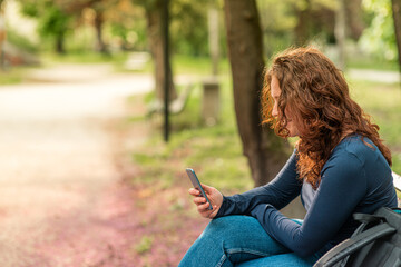 Portrait of charming red haired young woman with smartphone in a park