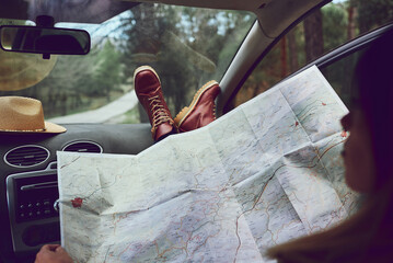 Woman sitting in her car looking at a map. She is in a forest.