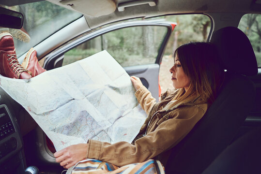 Woman sitting in her car looking at a map. She is in a forest.