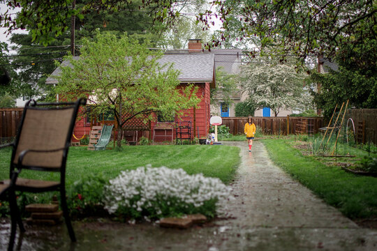 A small child walks down path in rain in backyard garden