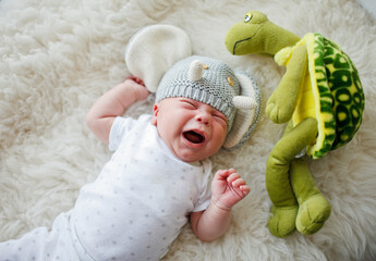 a newborn in a funny hat lays and cries