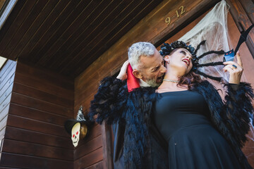 low angle view of man in halloween vampire costume biting neck of wife on cottage porch