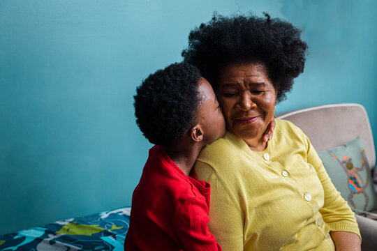 Grandson kissing grandmother on cheek by blue wall at home