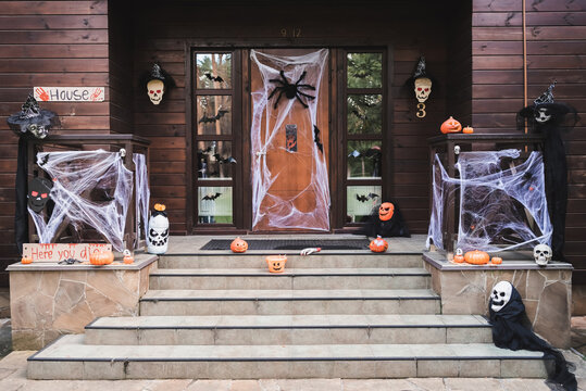 entrance of cottage decorated with carved pumpkins, spider net, toy spiders and paper cut bats