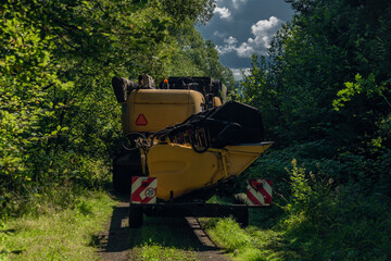 Yellow combine harvester on small path in sunny hot summer day