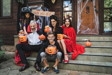 parents and kids in creepy halloween costumes grimacing while sitting on cottage stairs - obrazy, fototapety, plakaty