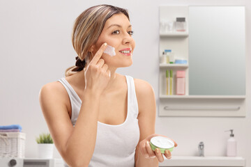 Young woman applying face cream in a bathroom
