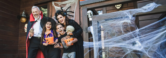 excited family in creepy halloween costumes laughing on porch with decoration, banner