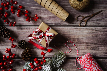 Christmas composition with holiday decoration, present, berries, cones, branches on dark wooden background. Festive holiday greetings. Holiday craft gift wrapping. Merry Christmas.