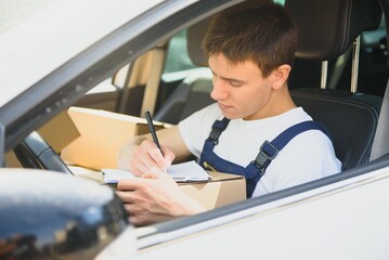 Young Delivery Man Checking List On Clipboard In car