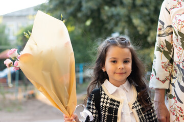 a little girl with long flowing hair and a large bouquet in her hands goes to school for the first time. First bell at school