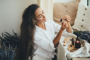 Young woman applying natural organic essential oil on hair and skin. Home spa and beauty rituals. - obrazy, fototapety, plakaty
