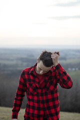 Fototapeta premium Candid portrait of a man in his 20s dressed in a black and red checked shirt looking into his future, immersed in his thoughts and contemplating. Authentic mood of a young man on an indecisive journey