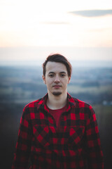 portrait of a twenty-three year old man in a black and red checked shirt, smiling at his friend with his real smile without any pretence. The authentic mood of a young man on an indecisive journey