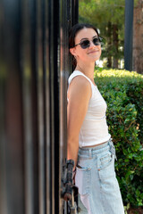 Confident female student on college campus standing with back against rod iron fence wearing sunglasses