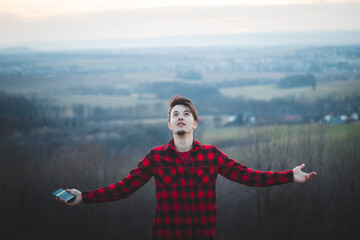 Candid portrait of a man in his 20s dressed in a black and red checked shirt joyfully facing the sky. He gives thanks to be on earth. Authentic people at their emotions