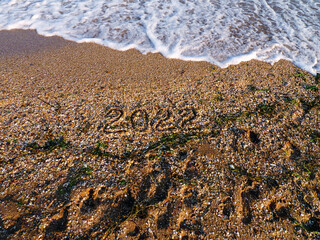 2022 written on sea sand. Sandy textured background. Wave with white foam. New year and Christmas concept. Template for greeting card, postcard, invitation, promotion, websites