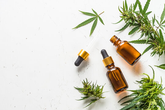 CBD oil and cannabis leaves at white table. Medicine and cosmetic product. Top view image with copy space.