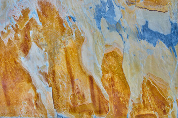 Rough stone texture with rust in blue and yellow colors with orange placed on a wall on a facade