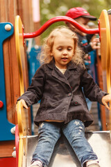 A cute blond child, girl having fun and sliding on outdoor playground, close up