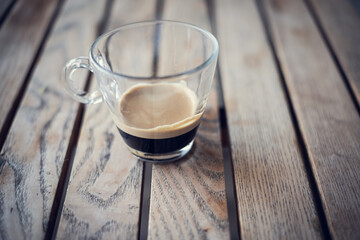 Short espresso coffee served on a transparent glass cup isolated on a striped wooden table