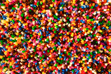 Fototapeta na wymiar Colorful small plastic beads forming the vivid background. Set of small multicolored, vivid craft elements. Concept of abundance. Artistic wallpaper, perfect for different designs.