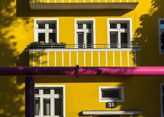 Yellow apartment building with a balcony and a pink water pipe 