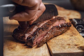 Cutting in slices flank steak on wood board