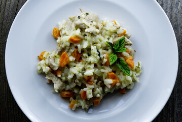 Top view of risotto with chicken, carrots and green basil on a white plate