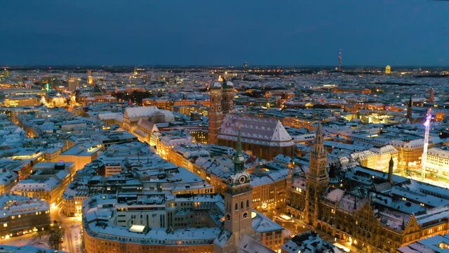 Munich aerial at night city covered with snow winer ambience, munich germany skyline drone video in 4k. Fly over marienplatz town hall and frauenkirche church.