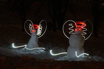 Kompozycja malowana światłem. Dwa bałwanki śnieżne z aureolami jak aniołki, zjeżdżają na nartach. © Tomasz