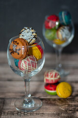 Elegant wine glasses filled with an array of vibrant macarons, poised on a wooden surface, oozing...