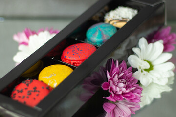 Luxurious assortment of macarons in a sleek tray complemented by delicate white and purple blossoms on a gray surface.