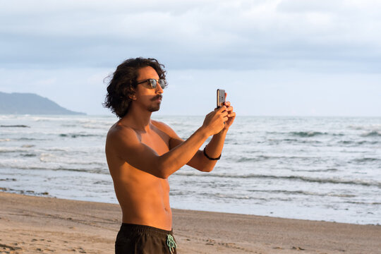 Man taking picture with phone at beach during sunset