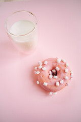 donut in pink glaze and a glass of milk on a pink background
