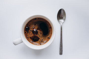 a cup of coffee with froth and a teaspoon on a white background