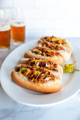 Close up of a plate of chili dogs with glasses of beer in background.