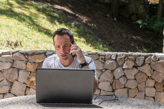 A man working at home outdoors using a laptop and talking on the cell
