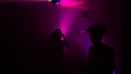 Silhouette image of people dance in disco night club to music from DJ on stage. Party atmosphere with disco ball. Nightlife concept. Space for text.